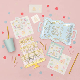 A pink and gold party kit with Let Them Eat Cake Large Napkins, cups, plates, and gold foil napkins for a tea party by Daydream Society.