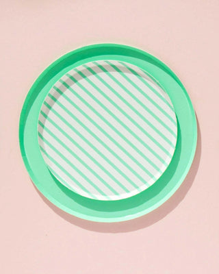 A Oh Happy Day Mint Stripe Plate - 7 inch rests on a pale pink surface, basking in soft light that casts a gentle shadow, evoking a simple, minimalist aesthetic.