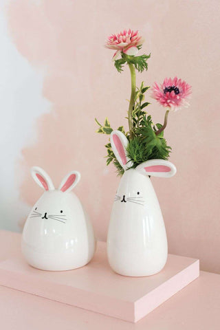 Two whimsical MINI BUNNY BUDVASE vases, hand-painted with intricate details, displayed on a pink shelf by Accent Decor.