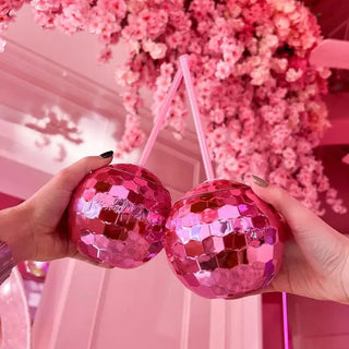 Two people holding Hot Pink Disco Drinks in front of a flower wall at a party. (Packed Party)