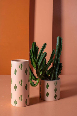 Two handcrafted ceramic cactus vases from Accent Decor, one standing vertically and the other lying horizontally, containing a green succulent plant against an orange background.